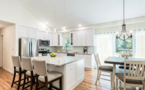 open kitchen with white cabinets and island and hardwood floors and angled ceiling and dining area with chandelier after renovation