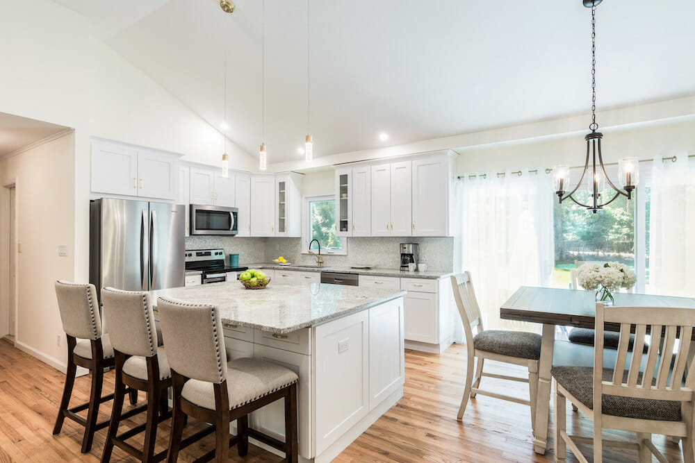 open kitchen with white cabinets and island and hardwood floors and angled ceiling and dining area with chandelier after renovation