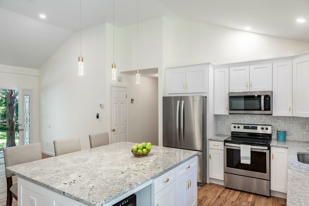 white kitchen cabinetss with stainless steel appliances and hardwood floor and island with granite countertop and pendant lights after renovation