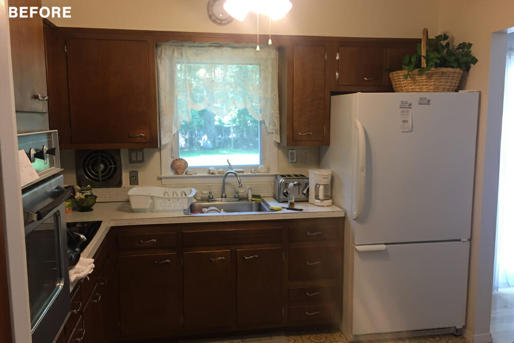 small kitchen with walnut cabinets and overmount stainless steel sink under a window and built-in oven before renovation