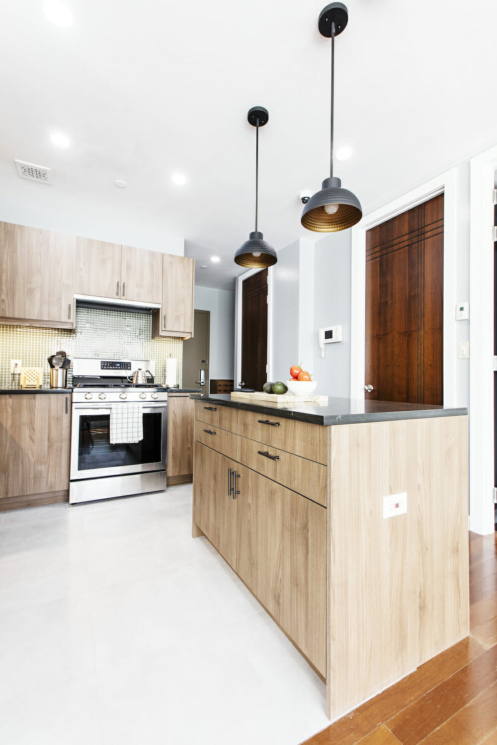 kitchen with natural wood cabinets and black granite countertop and island with pendant lights and white tiles on floor and recessed lighting after renovation