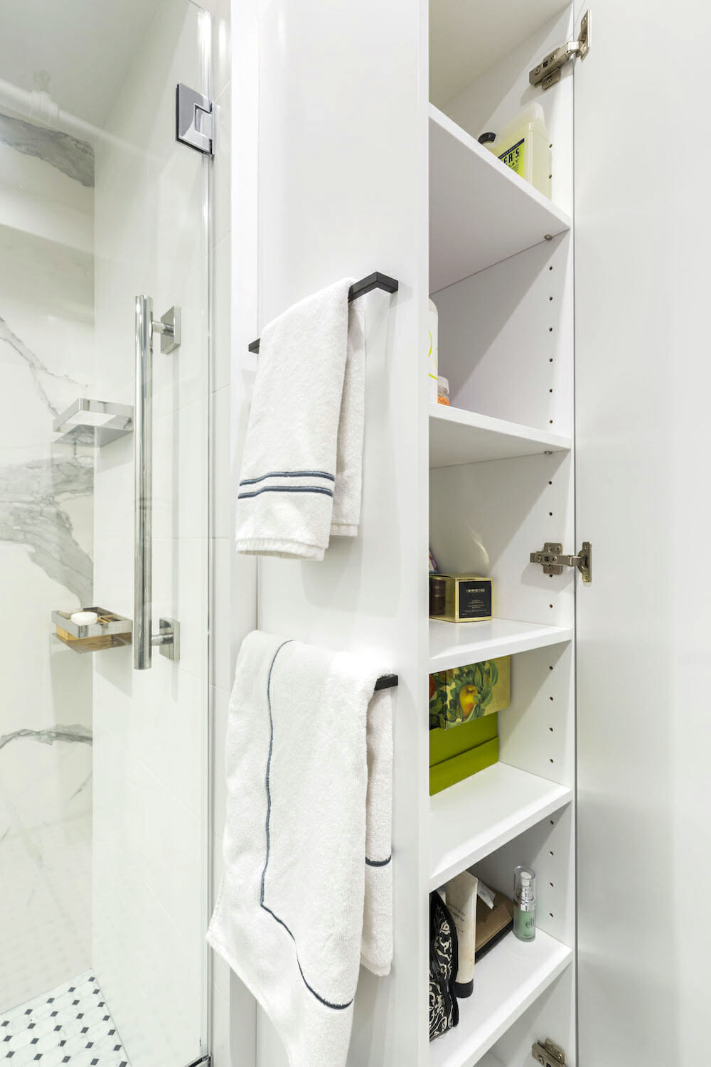 walk-in shower with marble tiles on walls and black and white flooring and built-in storage and black towel bars after renovation