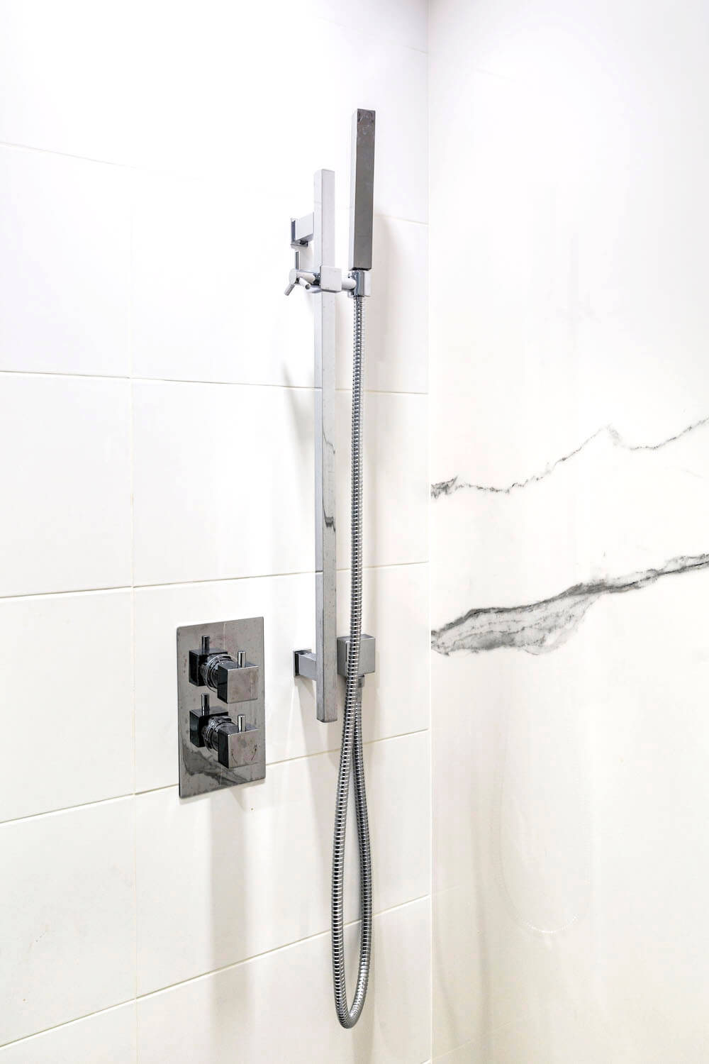 White porcelain shower tiles with white matte wall tiles and hand shower after renovation