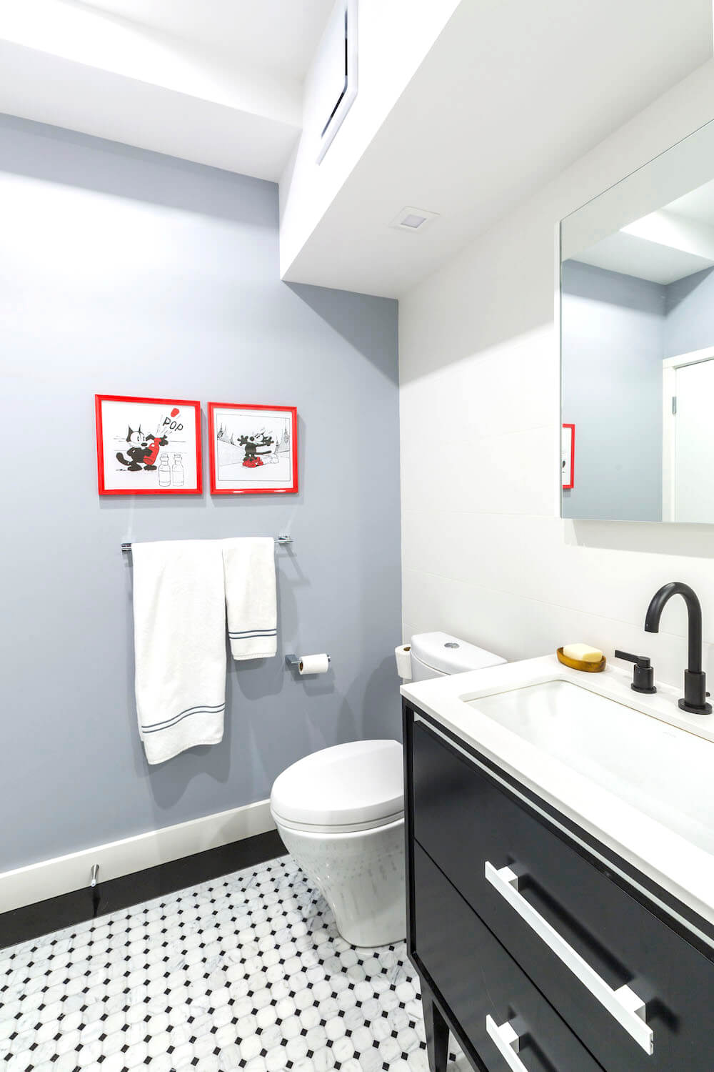 Blue wall in a white and black bathroom with white offset sink and black dot floor tiles after renovation