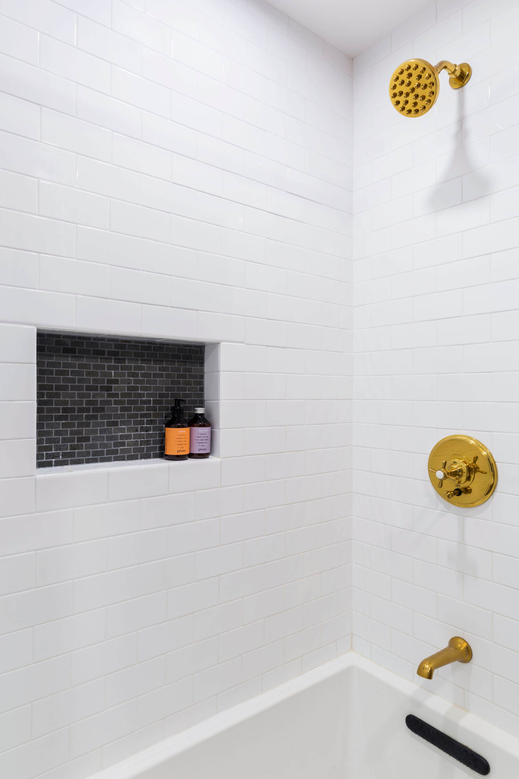 White subway tiles and little shower niche with brass shower head and shower valve over white bathtub after renovation