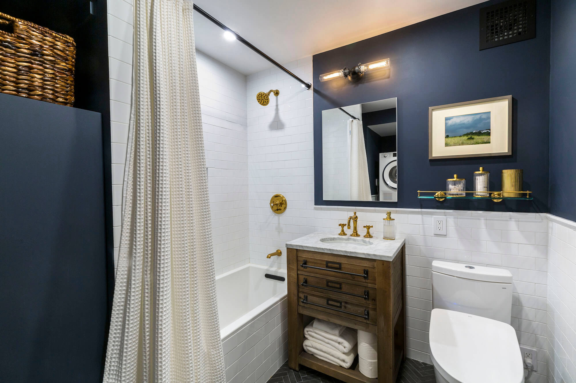 White subway tiles and navy blue wall paint in white bathroom with white bathtub and washstand after renovation