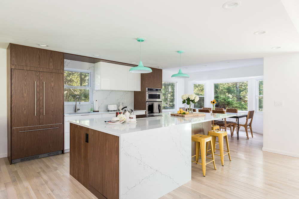 white kitchen island and closed brown kitchen cabinets and blue hanging pendant lights after renovation