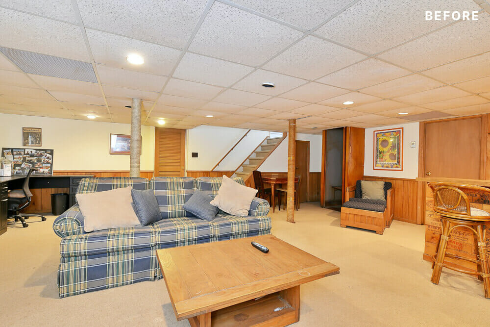 Beige carpeted basement with blue couch and furniture before renovation