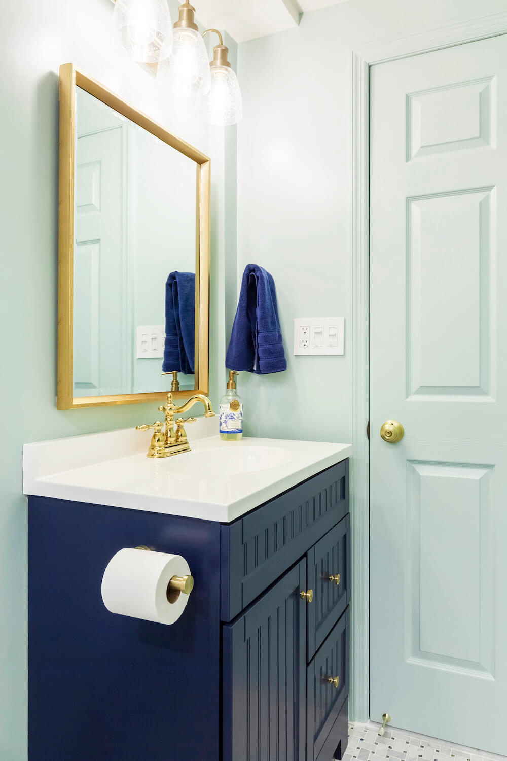 bathroom with navy blue vanity and gold mirror and pastel green walls and door after renovation