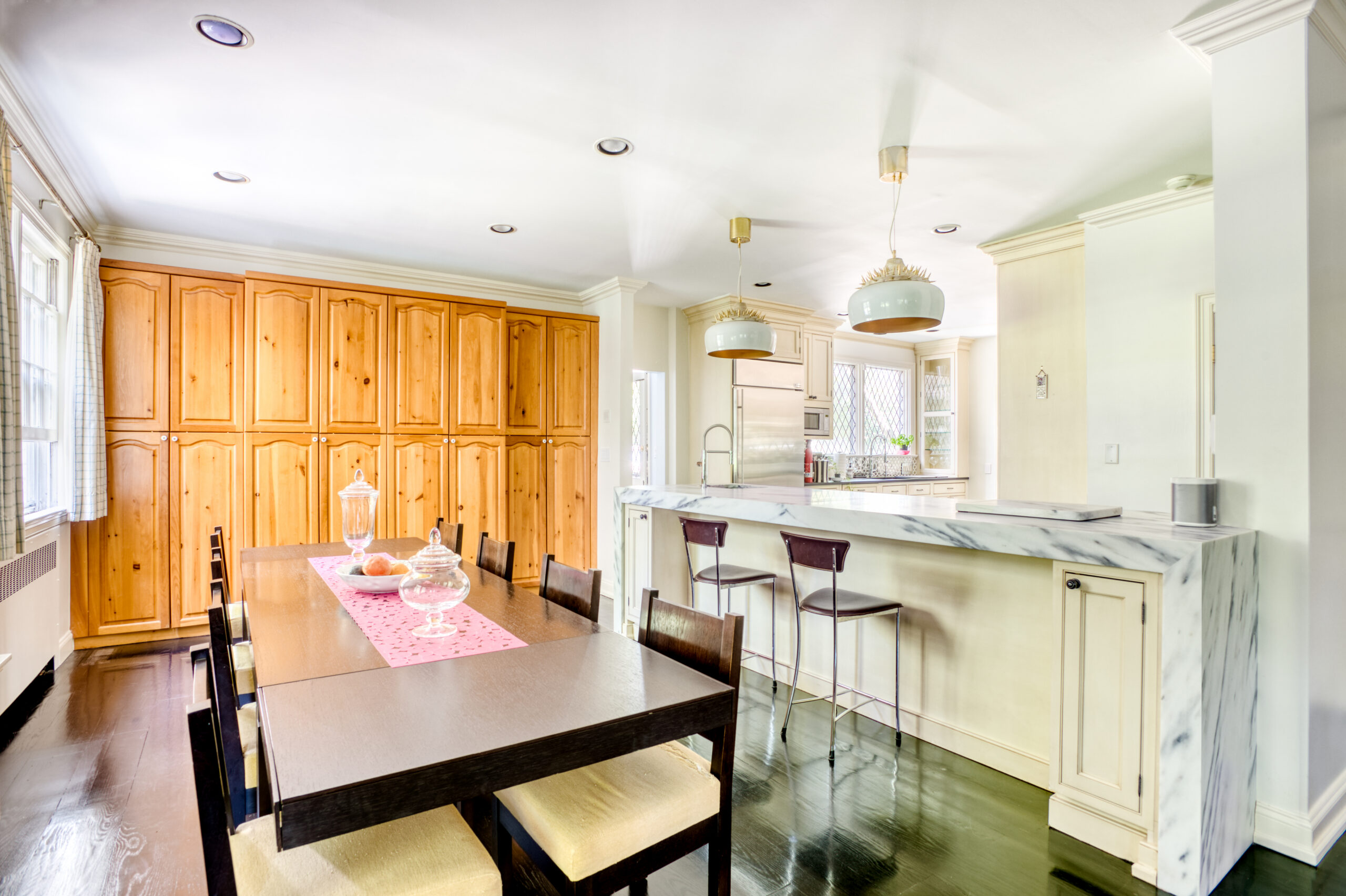 Westchester kitchen and dining area with retained wood cabinetry, a marble-wrapped peninsula, dark painted floors, and modern pendant lighting.