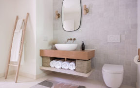 Beige and gray bathroom space with over counter wash basin and floating toilet after renovation