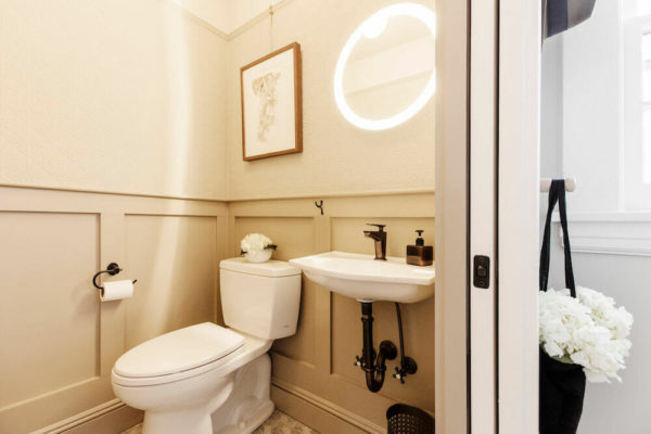 half bath with round mirror and wall paneling