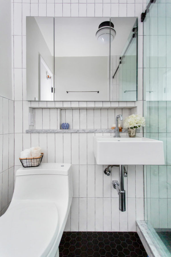 black hexagon floor tiles in a white bathroom with clear shower glass and white toilet after renovation