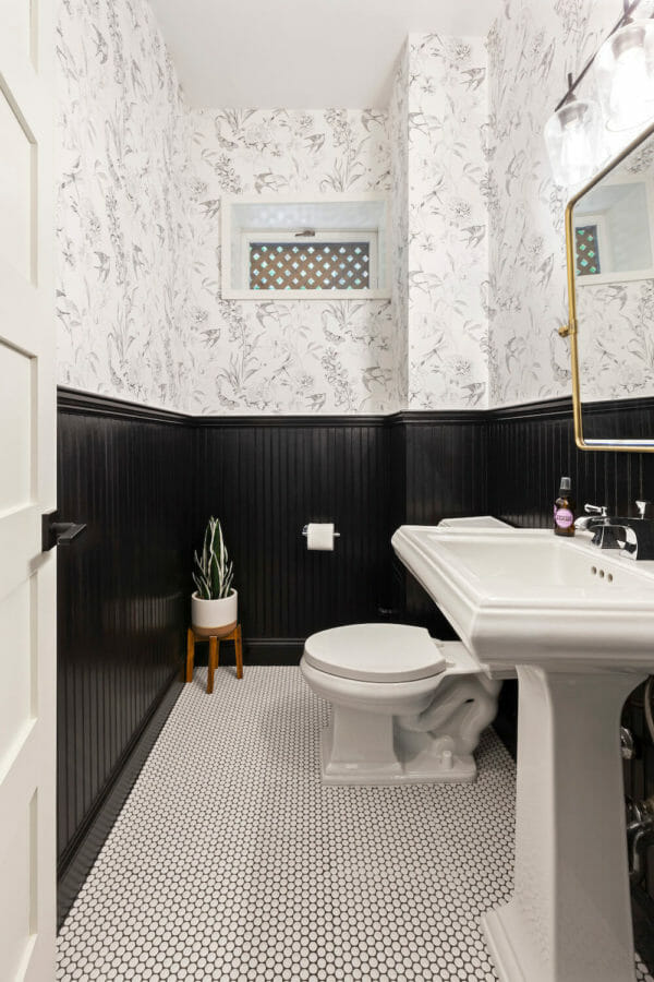 black half wall in a powder room with white pedestal sink and penny tiles after renovation