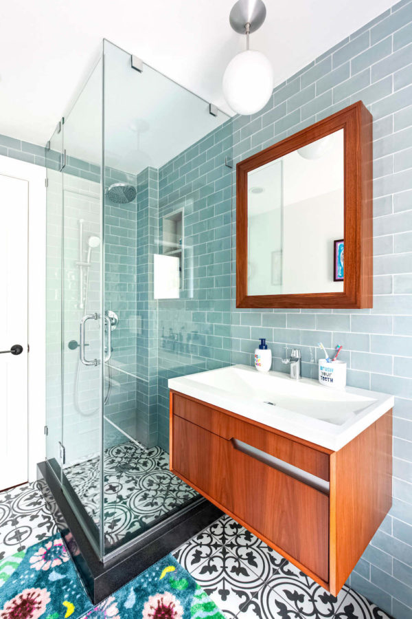 frameless clear glass shower door in a bathroom with blue wall tiles and patterned floor and floating vanity after renovation