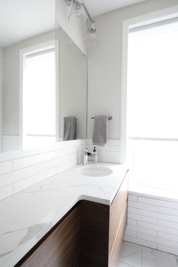 white subway tiles and gray wall in a bathroom with large mirror after renovation