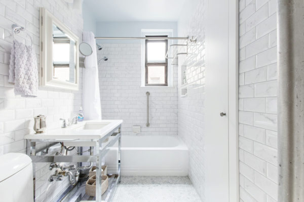 white subway tiled bathroom with white tub and grab bar and white sink after renovation