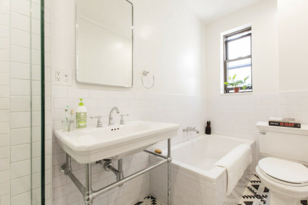white sink and white bathtub in a bathroom with patterned floor and double hung window after renovation