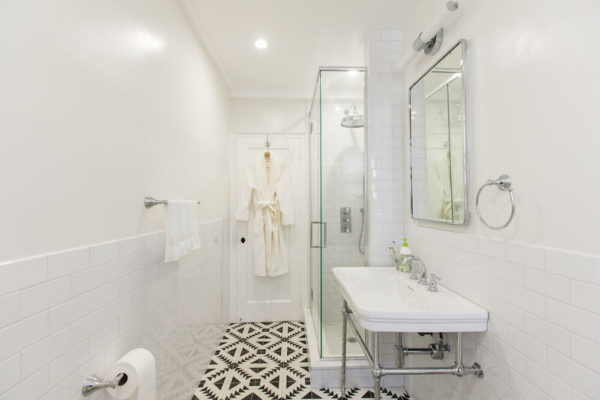 white bathroom with patterned floor tiles and glass separator and wide sink with mirror after renovation