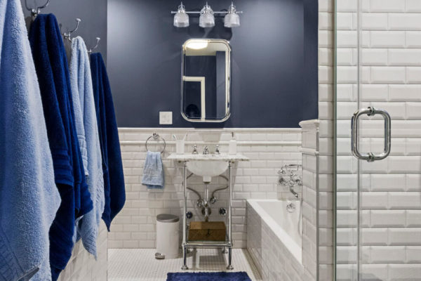 white bathtub in a white and blue bathroom with steel towel hangers and mirrored medicine cabinet after renovation