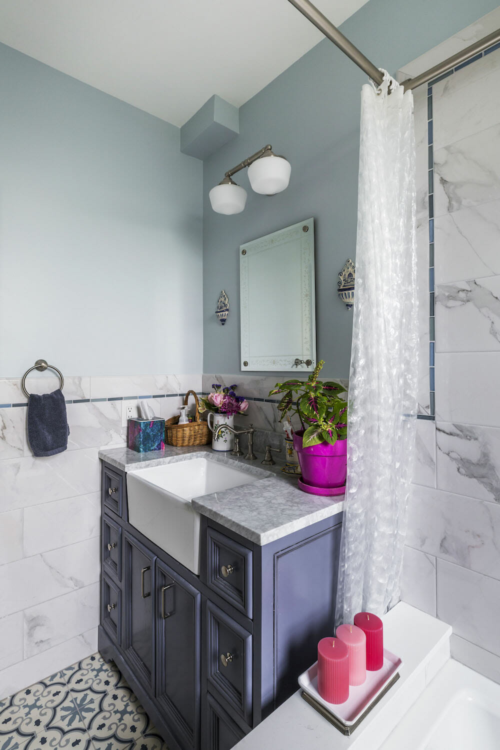navy blue single vanity with farmhouse sink and marble tiles on walls and countertop and sage paint on half walls and patterned floor tiles after renovation