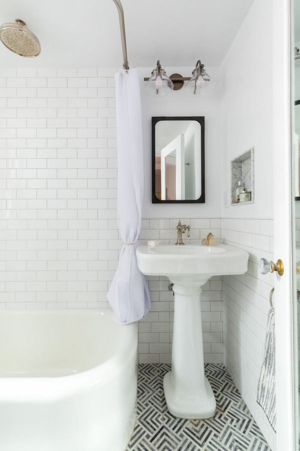 white pedestal sink in a small white bathroom with subway tiles and white bathtub after renovation