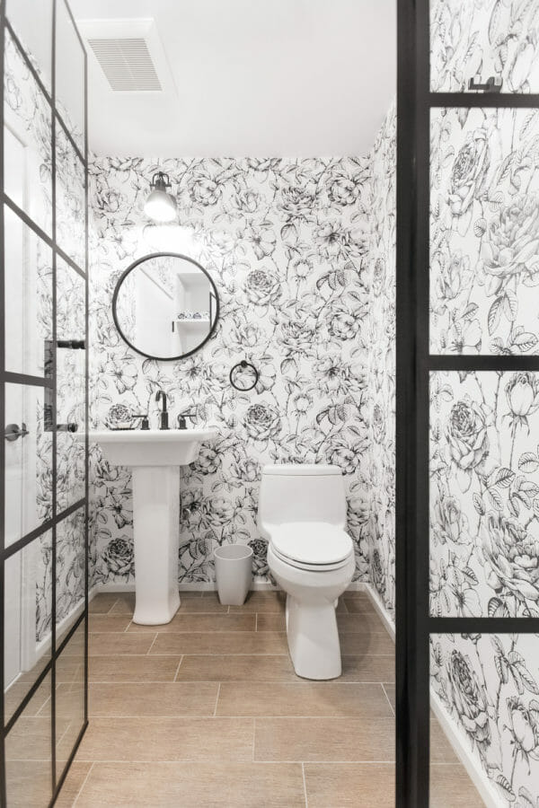 white bathroom with printed wall paper and pedestal sink and framed glass door after renovation