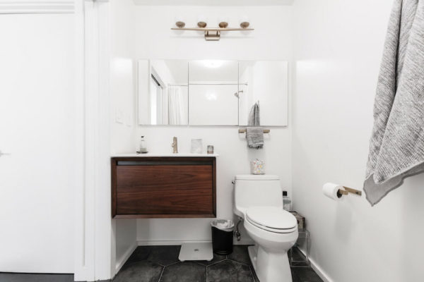 white bathroom with brown floating vanity and mirror with accent light after renovation