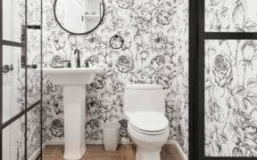black and white patterned wallpaper in a powder room with white toilet  and pedestal sink after renovation