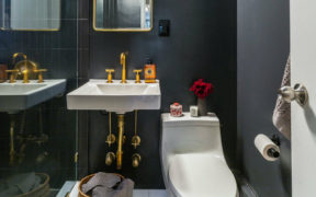bathroom with black walls and floating sink and toilet and gold faucets and fixtures after renovation
