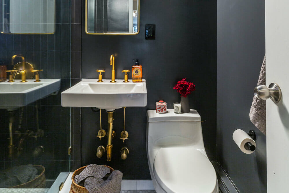 bathroom with black walls and floating sink and toilet and gold faucets and fixtures after renovation