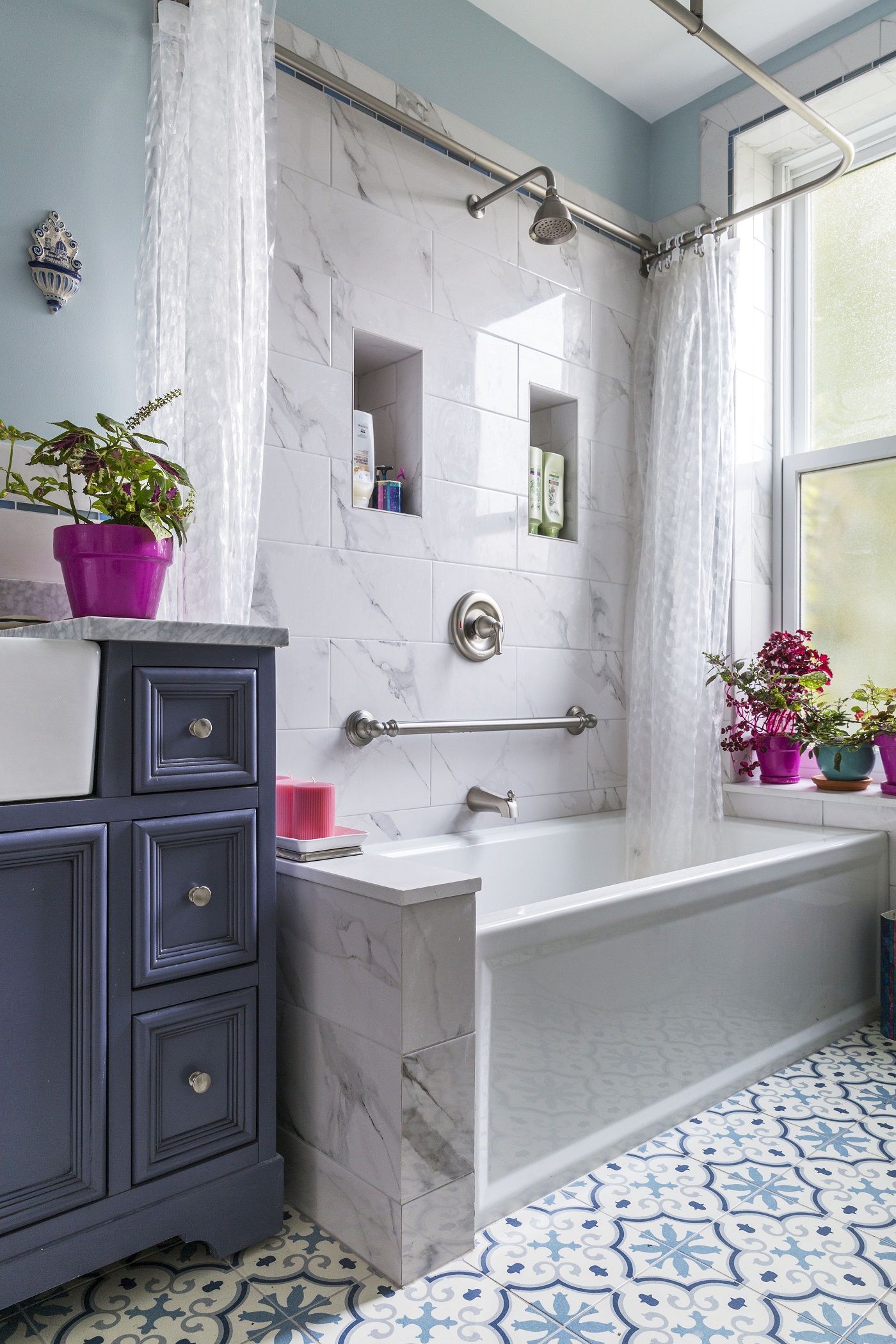 Boerum Hill bathroom remodel with white veined tub tile, two built-in shower niches, a grab bar, blue vanity, and patterned blue floor tile.