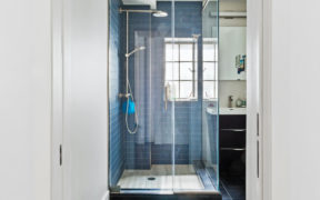 walk-in shower with frameless glass wall and black bathroom floor tiles and chrome shower head and fixtures after renovation