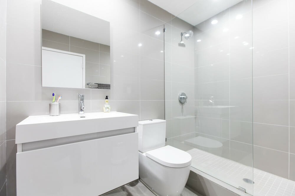 white bathroom with frameless glass separator for white bathtub and floating vanity after renovation