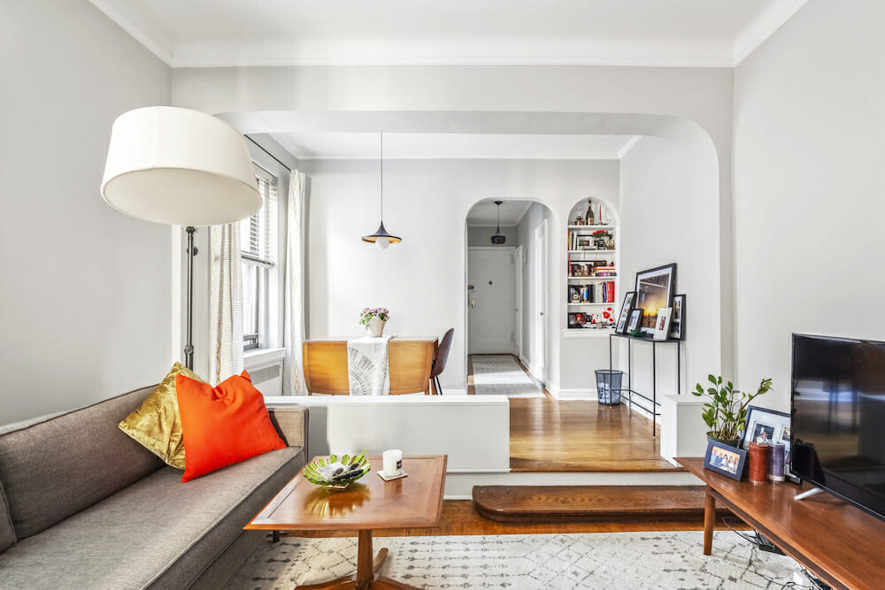 white living room with arched doorway and open recessed shelf on wallsand wooden flooring after renovation