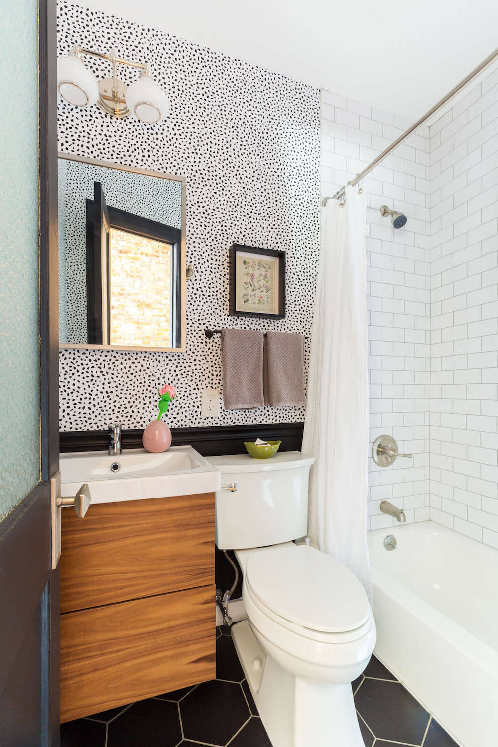 wallpaper in bathrooms with black hexagon tiles in a small bathroom with brown floating vanity and white bathtub after renovation