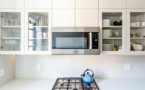 white kitchen cabinets with glass doors and white countertops with gas cooking range and white tile backsplash after renovation