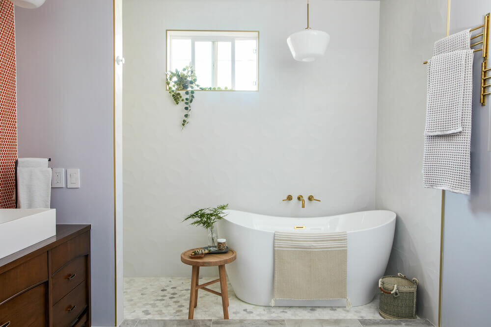 free standing bathtub with brushed gold faucet and fixtures and white and gray floor tiles and light gray walls and pendant light after renovation