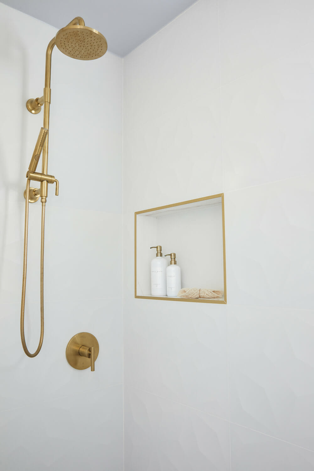 brushed gold shower head and fixtures and recessed shelf with gold frame after renovation