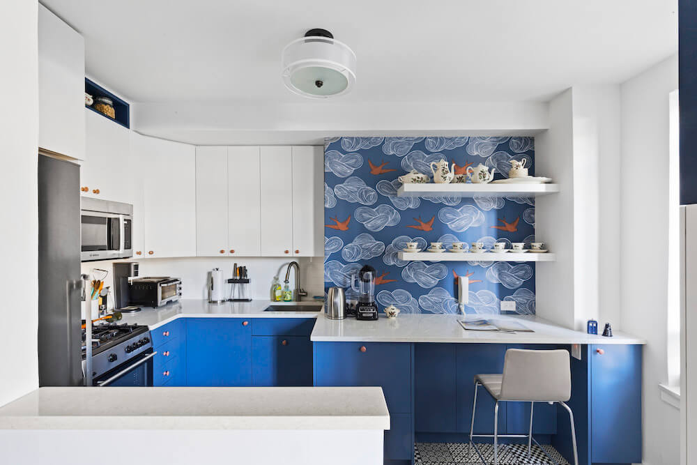 white island separator in a kitchen with blue cabinets and white countertop space along with blue wallpaper and open white shelves