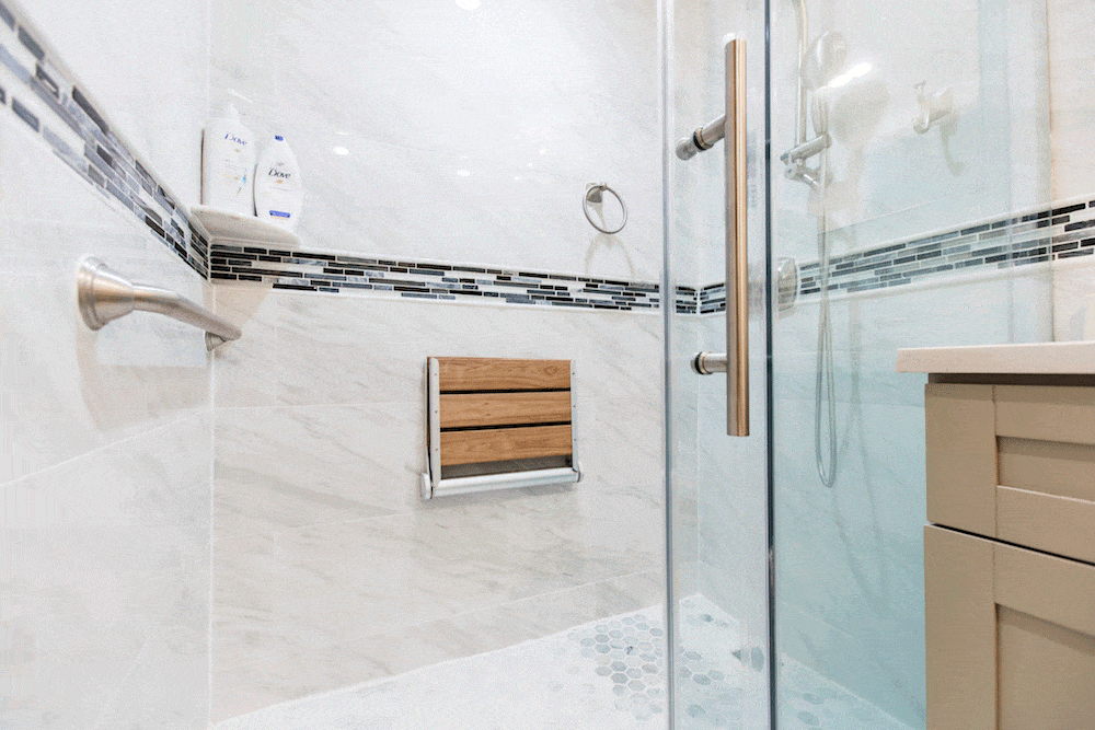foldable wooden seat and grab bars in a white bathroom with glass shower door with handles after renovation