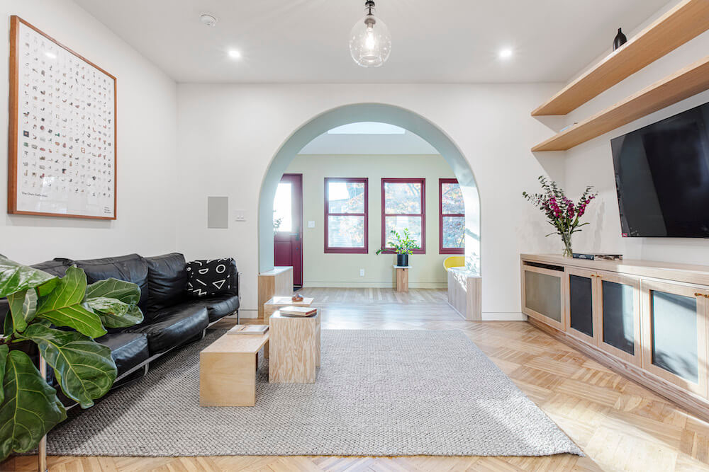 Modern living room with pale hardwood floors, open shelves and arched entryway