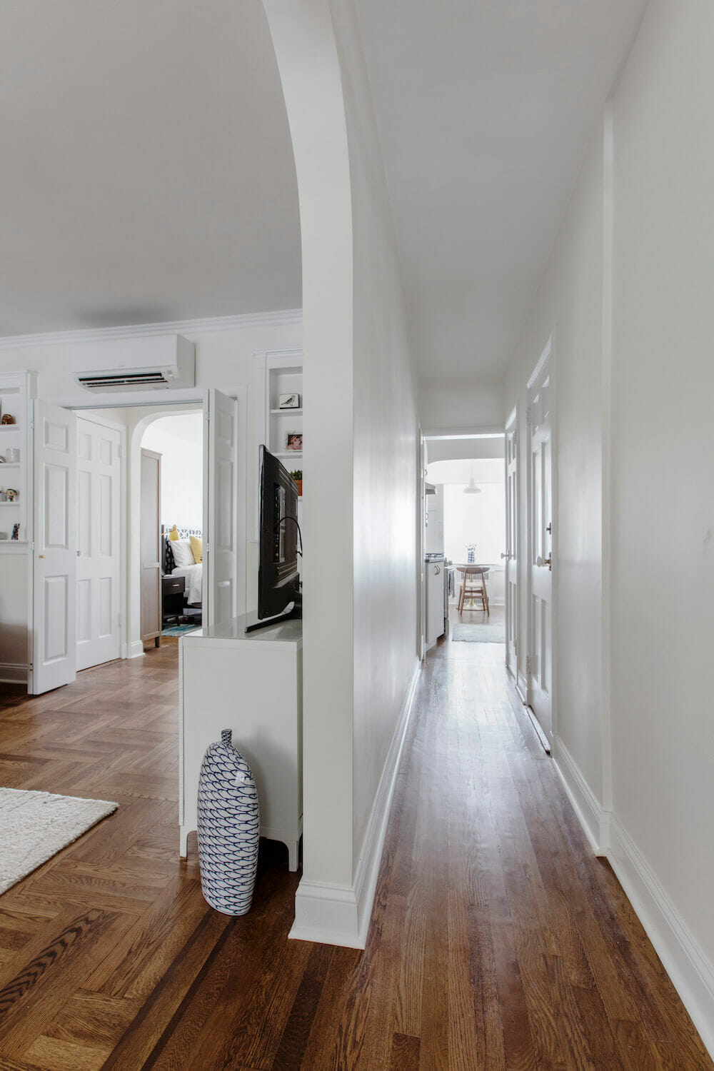 white room separator with passageway to room on one side and the living room on another with brown floor tile after renovation