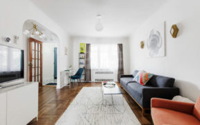 white living room with blue and red couch and white floor rug on wooden floor and large window after renovation
