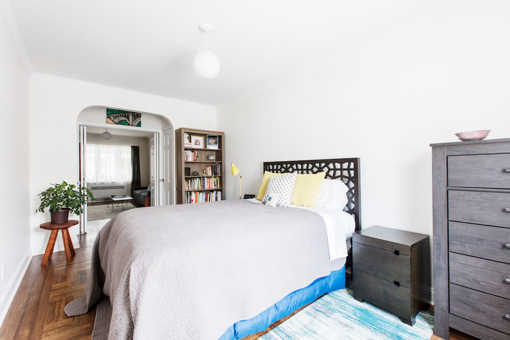 white bedroom with gray chest of drawers and large bed with gray bed cover in a wooden floor after renovation