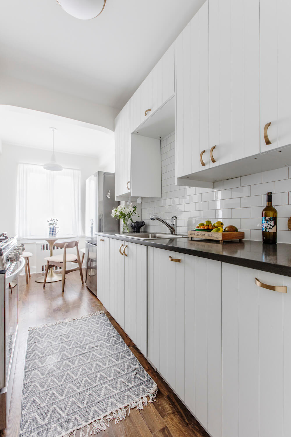 white open kitchen with closed kitchen cabinets and golden handles and white backsplash after renovation