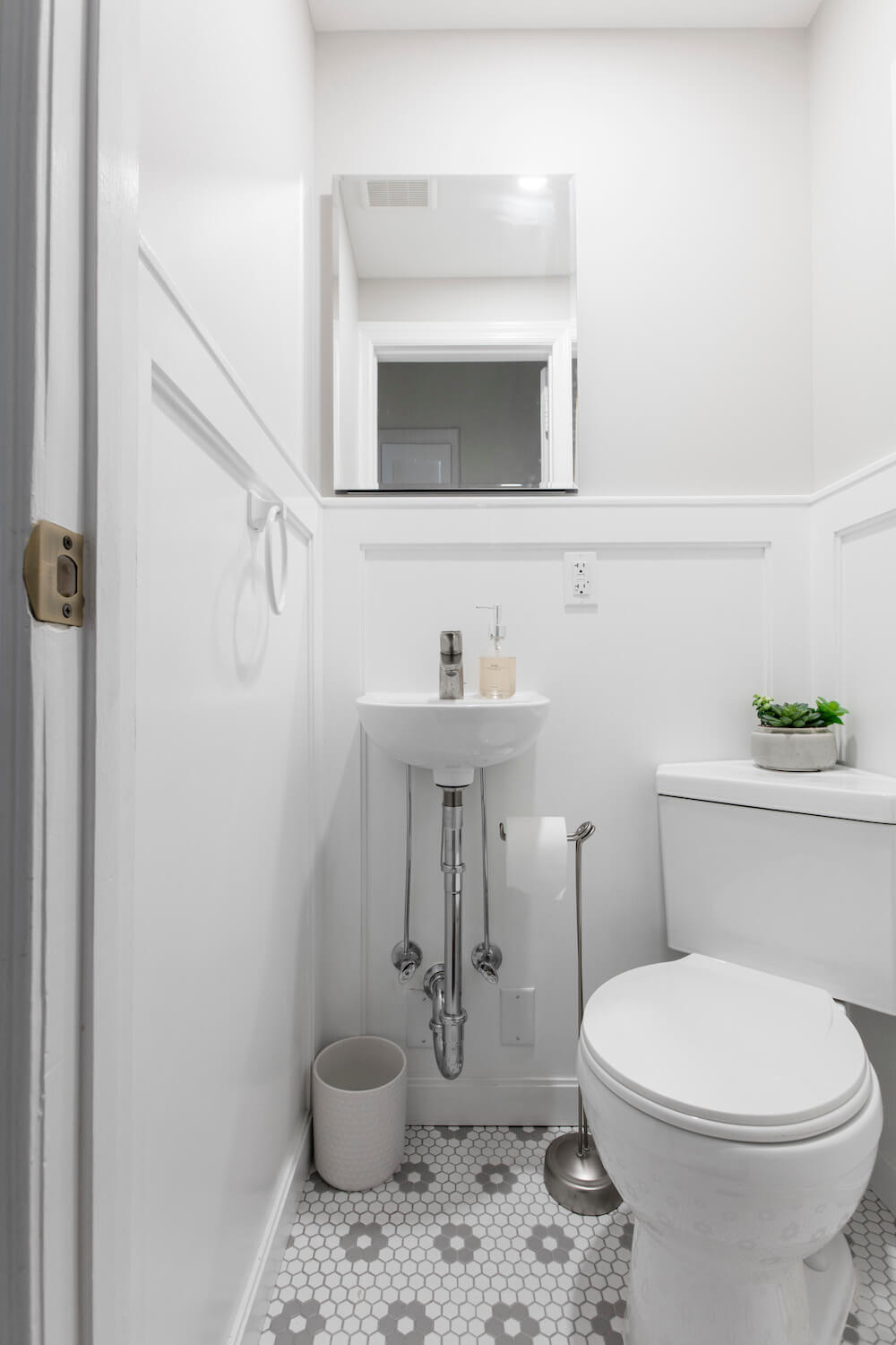 small white bathroom with white toilet and white sink on gray patterned floor after renovation