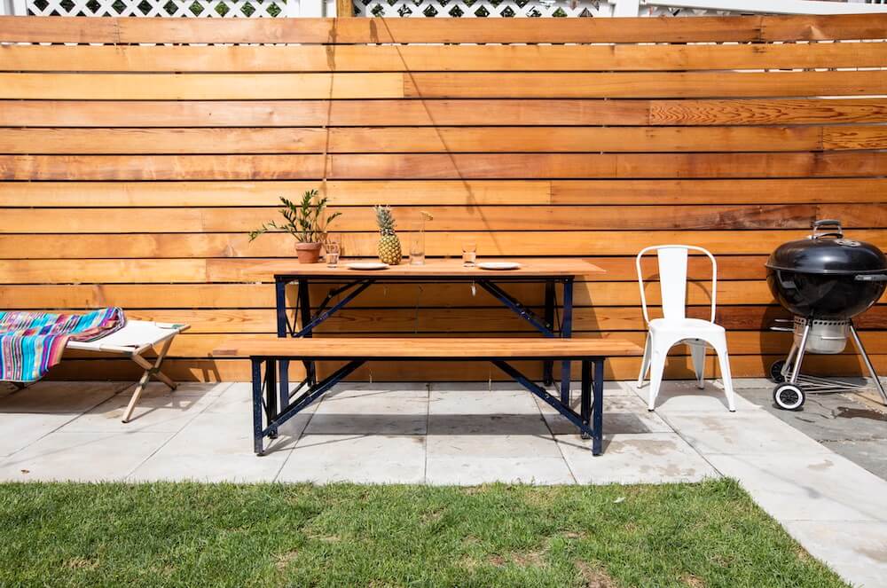 Brown outdoor table and bench seating with white chairs and a grill after renovation