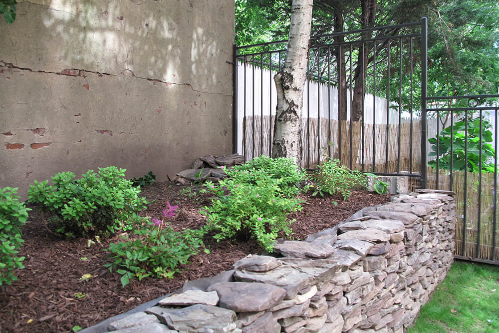 stone wall and flower bed along with black railing on metal gate before renovation