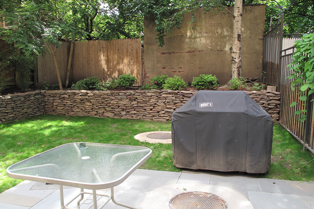 covered barbeque grill in a backyard with green grass and white table before renovation